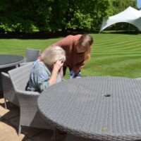 lady sitting feeling ill with a standing female looking concerned in a garden